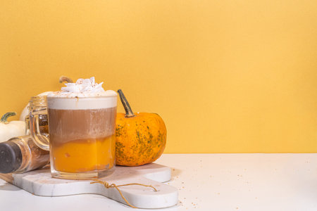 Glass cup with tasty pumpkin spice latte, with white and orange pumpkin squash, pumpkin pie spices and autumn decor copy space. Traditiional autumn Thanksgiving holiday drinkの写真素材