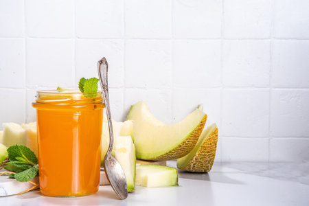 Sweet melon jam, homemade jelly preserves in small glass jar with fresh melon slices on white marble tableの写真素材
