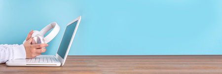 Notebook computer laptop, with headphones for  music, woman hands in picture. Distant learning, working from home, online courses, pc support, listening audio podcast, blogger table bannerの写真素材