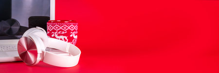 Festive red composition with white laptop computer, headphones, big cup for hot chocolate. Christmas mood and vibe, listen traditional new year songs music. Preparation for Christmas backgroundの写真素材