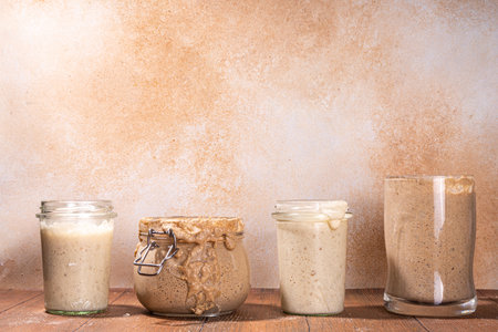 Healthy lifestyle, gluten free fermenting diet. Homemade sourdough. Active bubbly rye, wheat, oat sourdough with different flour and fermentation methods, in glass jars, with raw dough and baked breadの写真素材