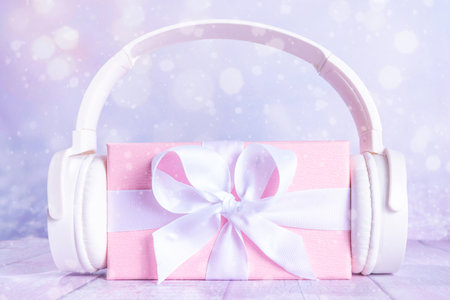 Beautiful still life composition with pink white gift box and headphones on table on snowy blurred lights background. Christmas music conceptの写真素材