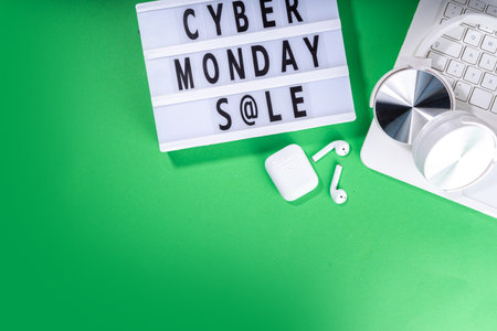 Cyber monday sale background. Simple bright green flat lay with lightbox "Cyber monday", gift boxes, shopping cart, laptop, tablet, headphones top view copy space. Online holiday shopping conceptの写真素材