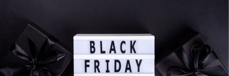 Black friday sale background. Simple black flat lay with sign "Black friday", gift boxes, shopping cart, laptop, tablet, headphones top view copy space. Online Black friday shopping conceptの写真素材