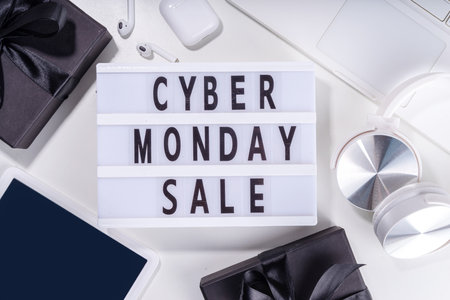 Cyber monday sale background. Simple white flat lay with lightbox "Cyber monday", gift boxes, shopping cart, laptop, tablet, headphones top view copy space. Online holiday shopping conceptの写真素材