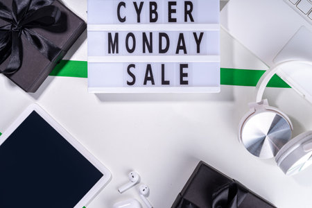 Cyber monday sale background. Simple white flat lay with lightbox "Cyber monday", gift boxes, shopping cart, laptop, tablet, headphones top view copy space. Online holiday shopping conceptの写真素材