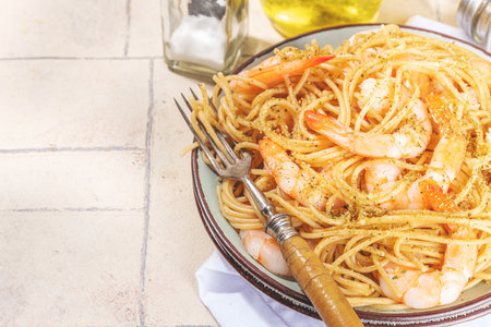 Italian durum, buckwheat, gluten-free dark colored spaghetti pasta with fried shrimp prawns and herbs, on beige tiled backgroundの写真素材