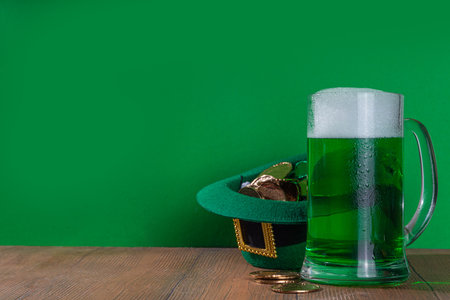 Beer glasses with leprechaun hat, shamrock clover leaves, traditional decorations for St. Patrick's Day, on green wood background. St. Patrick's Day Ireland holiday greeting card, invitation backgroundの写真素材