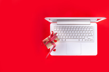 Valentine day simple background, Woman using laptop, with gift bow with festive tied ribbon, heart decor, on bright red background. Online Valentine`s shopping, preparation for February 14 holiday.の写真素材