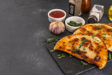 Chebureks, empanadas. Fried pies pasties, with meat and spices, on a black concrete background with...