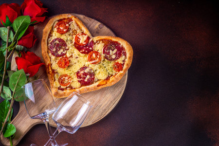 Heart shaped pizza with tomatoes and mozzarella and pepperoni on dark table background. Idea for Valentine day dinner, dating, lunch or dinner February 14 menu for couples, top view copy spaceの写真素材