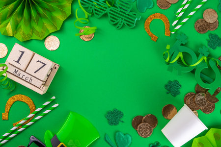 Happy Patrick's Day greeting card party invitation. Accessories for St Patrick holiday leprechaun hat, glasses, shamrock, gold coins, block calendar March 17 date, ornaments, green background top viewの写真素材