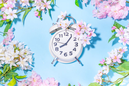 Spring Time Change background. Beautiful fresh spring tree flowers with alarm clock on light blue...