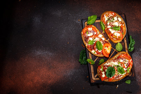 Hot loaded pizza sandwiches with tomatoes, mozzarella cheese and pepperoni, on dark background with herbs, olive oil and spicesの写真素材
