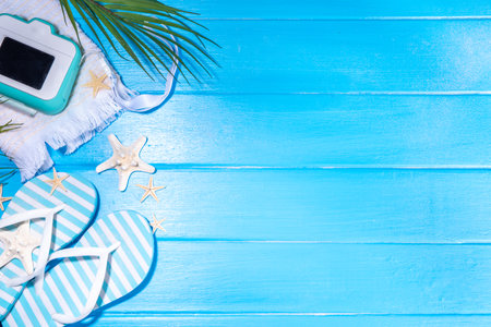 Bright sunny lighted summer vacation background, vacation and travel, beach accessories, swim suit, hat, flip flops, photo camera, sea star and shells on high-colored blue wooden background top viewの写真素材