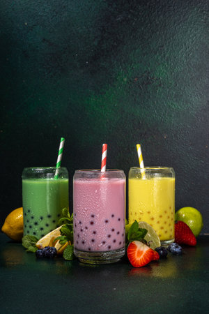 Set of three colorful summer bubble tea, bright creamy pearl tea or latte tapioca drinks, pink berry, yellow citrus, green mint, with tapioca balls and crushed ice, on dark backgroundの写真素材
