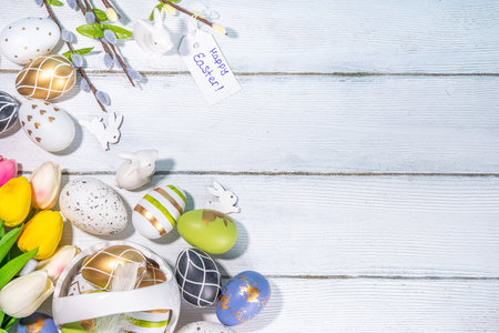 Spring Easter holiday greeting card background. Willow spring flower branches, colorful green, golden Easter eggs in basket, with tag Happy Easter on white wooden background top view copy spaceの写真素材