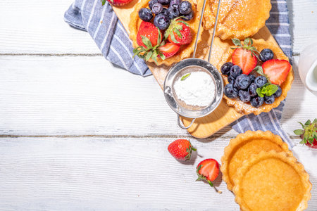 Sponge mini tart cakes with summer berry. Portioned vanilla dessert cups with fresh strawberry, blueberry, raspberry, on white wooden background copy spaceの写真素材