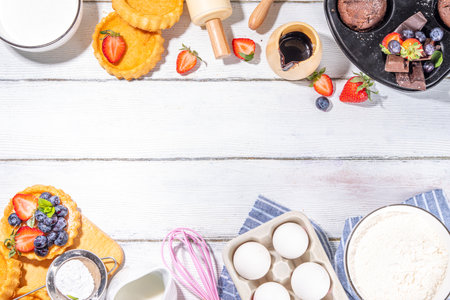Summer baking background with baked pastry - berry cakes, muffins, mini pie tarts, with cooking baking ingredients, flour, eggs, rolling pin, cream milk, sugar, strawberry, white wooden backgroundの写真素材