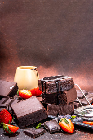 Dark chocolate brownies with berries. Stack of homemade brownie cake cookies with chocolate sauce drizzled on it and fresh strawberry, blueberry, on dark background copy spaceの写真素材