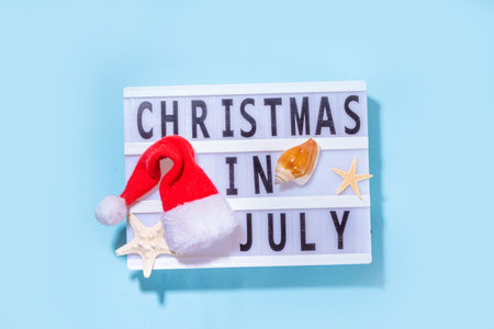 Christmas in July summer holiday or sale background. Summer vacation accessories, seashells, Starfish, lounge chair with Santa hat, tropical leaves. Getaway during winter holiday, top view copy spaceの写真素材