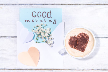 Coffee mug with bouquet of white flowers and notes Good morning on wooden table, beautiful spring breakfast concept, top view flatlayの写真素材