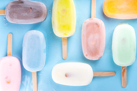 Selection of multicolored ice creams. Various flavor gelato, frozen lollypops - chocolate vanilla blueberry strawberry pistachio orange, on light blue backgroundの写真素材