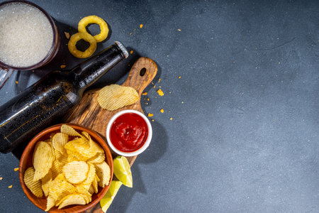 Beer with various salted snacks set. Black table background with traditional party snacks, beer bottles and glasses, with chips, onion rings, salted nuts, crisps and sauces top view copy spaceの写真素材