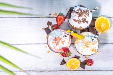 Set of summer refreshing milkshakes or smoothies with classic delicious taste - vanilla lemon, strawberry, chocolate, with whipped cream and toppings, On a white wooden light blue sunny backgroundの写真素材