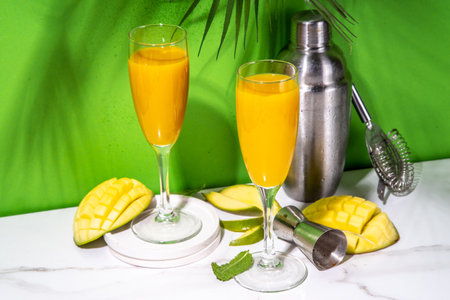 Mango mimosa or  bellini cocktail, summer refreshing cool fruit drink with fresh sliced mango garnish on , on high-colored backgroundの写真素材