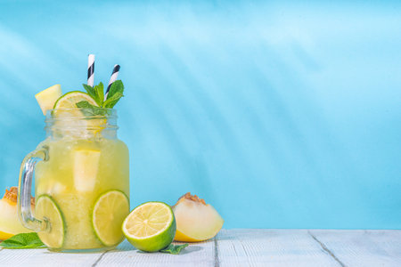 Melon lemonade or mojito, melon and lime juice, with crushed ice, fruit slices garnished with mint leaves. Fresh organic summer drink, infused fruity water mocktail, on high-colored sunny backgroundの写真素材