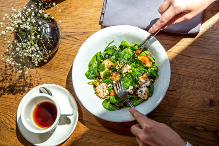 Close-up lifestyle girl in restaurant eat salad with greens, vegetables, balsamic sauce, on terrace, hands in picture. Healthy lunch, food delivery, cafe menu. Break for energy, vitamins, refreshnessの写真素材