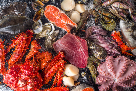 Set of various fresh raw seafood - octopus, crab, squid, shrimp prawn, oyster, mussels, salmon tuna dorada fish with spices of herbs lemon, black background with crushed ice copy space top viewの写真素材