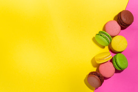 Bright colorful (yellow, pink, green, brown) various flavor macarons sweet cookies on high-colored pink yellow background.  Stack of small french macaron cakes, copy space flatlayの写真素材