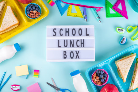Healthy school meal, children packed lunch box with fruit, berry, nuts and sandwich with vegetables. Kids diet snack food with education school supplies, bright blue background top view copy spaceの写真素材