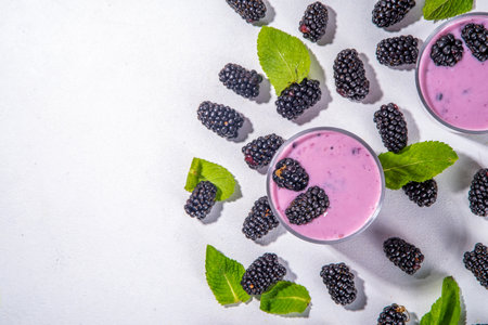 Two glasses of blackberry smoothie, yogurt or milkshake with fresh berry, mint leaves on white table background copy spaceの写真素材