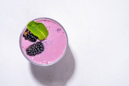 Two glasses of blackberry smoothie, yogurt or milkshake with fresh berry, mint leaves on white table background copy spaceの写真素材