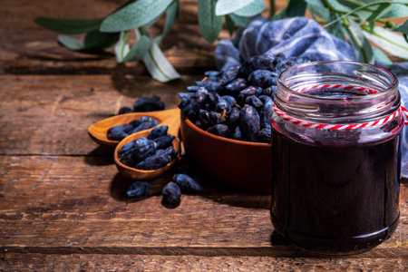 Small glass jar with homemade  haskap berry jam, on wooden background with bowl of fresh haskap (honeysuckle, honeyberry) berries, copy spaceの写真素材
