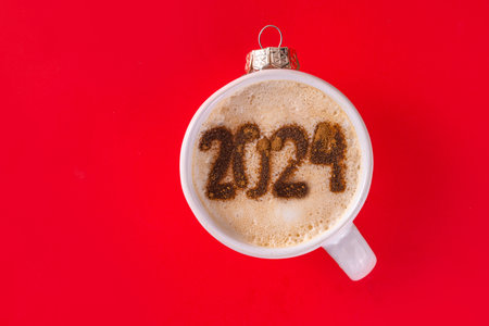 New year Christmas flat lay with festive decorated coffee or hot chocolate with latte art drawing 2024. Holiday hot drink mug as Christmas tree ball, with ornaments, decor on red background top viewの写真素材