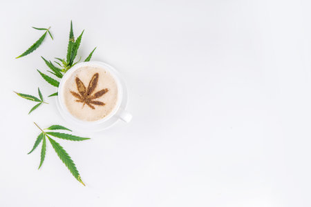 Medical cannabis hemp coffee latte. Cup of creamy whipped coffee with cannabis oil drops and leaf drawn top , with hemp leaves on white backgroundの写真素材