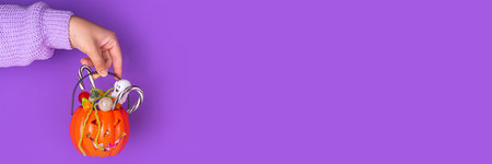 Woman or kid hands holding jack-o-lantern bucket full with candies. Children Halloween trick or treat party background, having fun at  trick or treating, halloween invitation, sale or greeting cardの写真素材