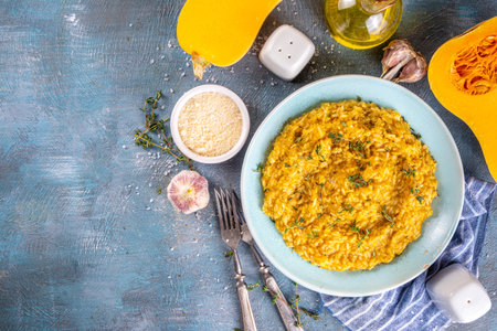 Delicious homemade cheesy puff pumpkin risotto with parmesan cheese and thyme, with ingredients and spices on blue concrete tableの写真素材