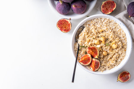 Breakfast autumn morning oatmeal. Bowl of oatmeal with fresh figs and nuts, on white kitchen background copy spaceの写真素材