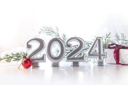 2024 New Year holiday background with numbers 2024, gift box, christmas tree decoration and baubles, festive lights and fir tree, gold silver background copy spaceの写真素材