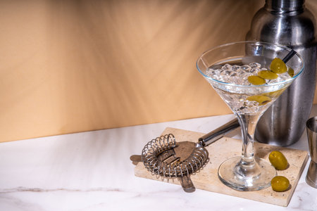 Classic dry martini cocktail with green olive garnish, on high-colored beige backgroundの写真素材