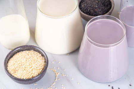 Black and white sesame milk, Alternative vegan non-dairy milk drink on glass and bottles with sesame seeds on light stone background. Raw food, vegetarian natural organic food dietの写真素材
