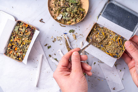 Alternative healthy berbal smoking blend. Handmade craft cigarette, preparation process, with mixture of herbs, leaves and flowers, with boxes, paper, on white backgroundの写真素材