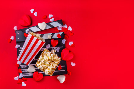 Romantic date on Valentine's Day February 14. Love movie marathon, date at cinema theater. Clapperboard, popcorn buckets, heart decor and chocolates on red background flat lay copy spaceの写真素材