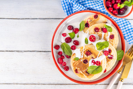 Sweet cranberry pancakes for winter breakfast or brunch. Festive Christmas, New Year breakfast dessert with vanilla creamy topping and fresh cranberries, copy spaceの写真素材