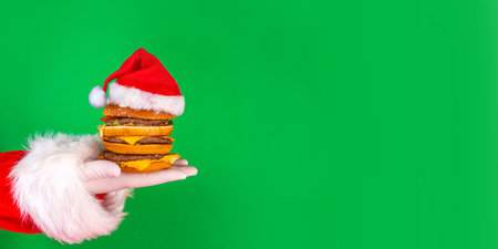 Christmas burger and french fries delivery menu. Santa hands with big tasty cheeseburger with french fries and ketchup sauce on festive Christmas and New Year decorated backgroundの写真素材